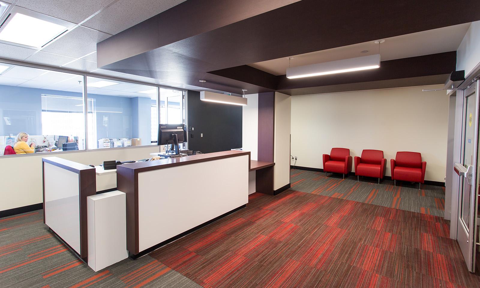 SAFE Work Manitoba. Reception desk showing adjoining office and a row of three red chairs in waiting area.